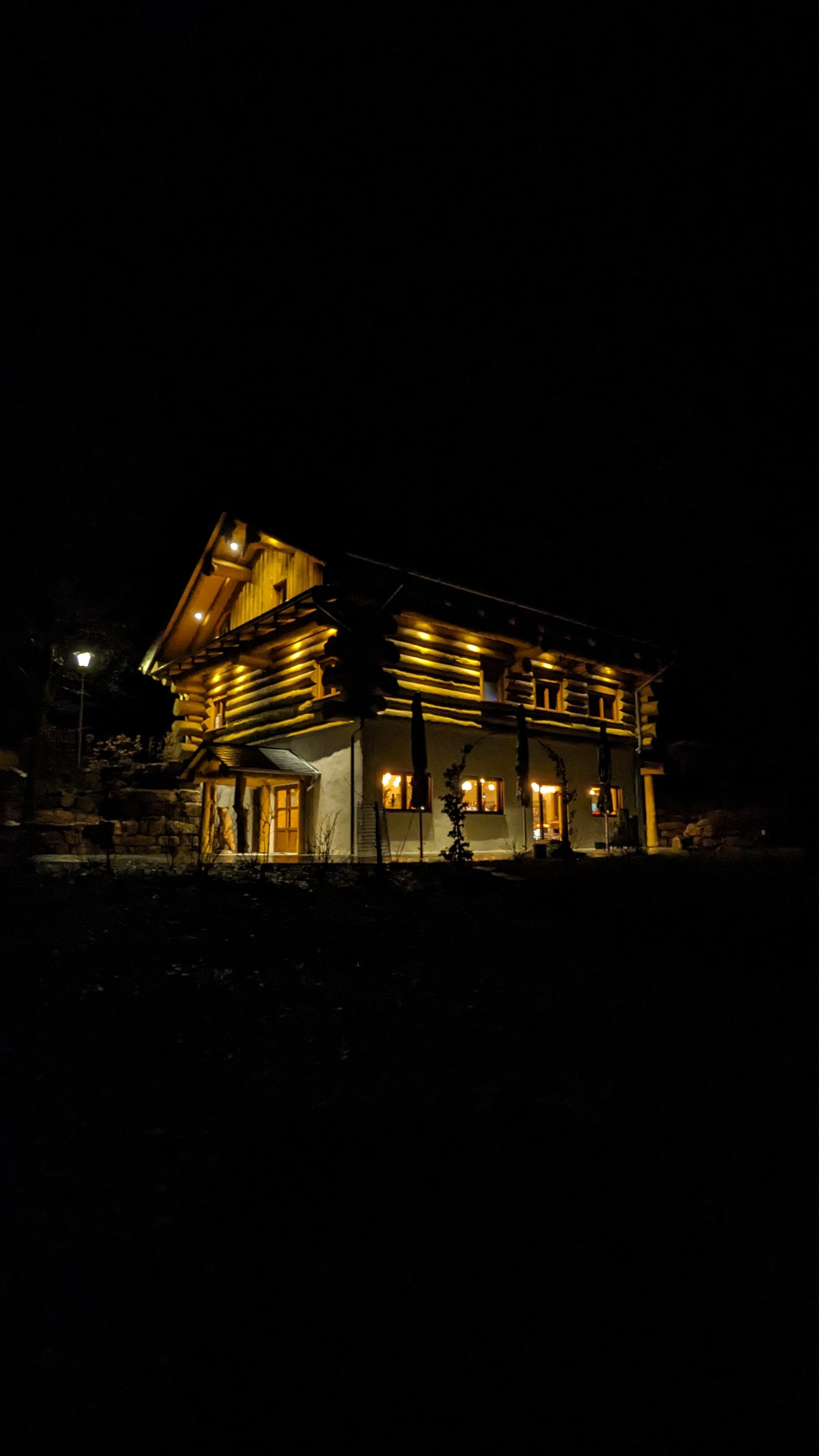 Das Waldzeit-Blockhaus bei Nacht, stimmungsvoll beleuchtet mit warmem goldenen Licht vor schwarzem Hintergrund.